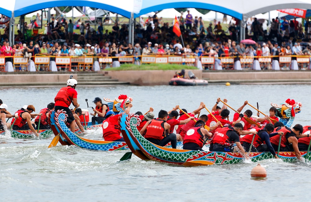 Athletes pulling vigorously on the oars in a competitive boat racing on Keelung River & spectators on the riverbank cheering for their teams in the traditional Dragon Boat Festival in Taipei, Taiwan