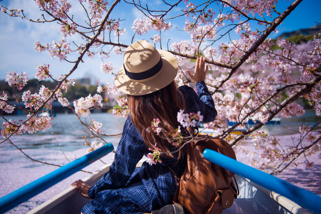 Hipster woman is sightseeing cherry blossom on the row boat while traveling during spring season at Chidorigafuchi boat parking inside the Kitanomaru Park in Tokyo, Japan.